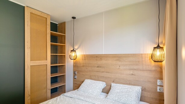 Un dormitorio con cabecera de madera, dos lámparas de noche y una cama con ropa de cama estampada.