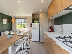 Una cocina moderna con comedor, armarios blancos, estufa integrada y ventana con vistas a zonas verdes.