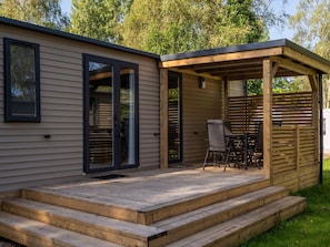 Eine Holzterrasse mit Tisch und Stühlen, ein überdachter Patio-Bereich und eine Glasschiebetür.