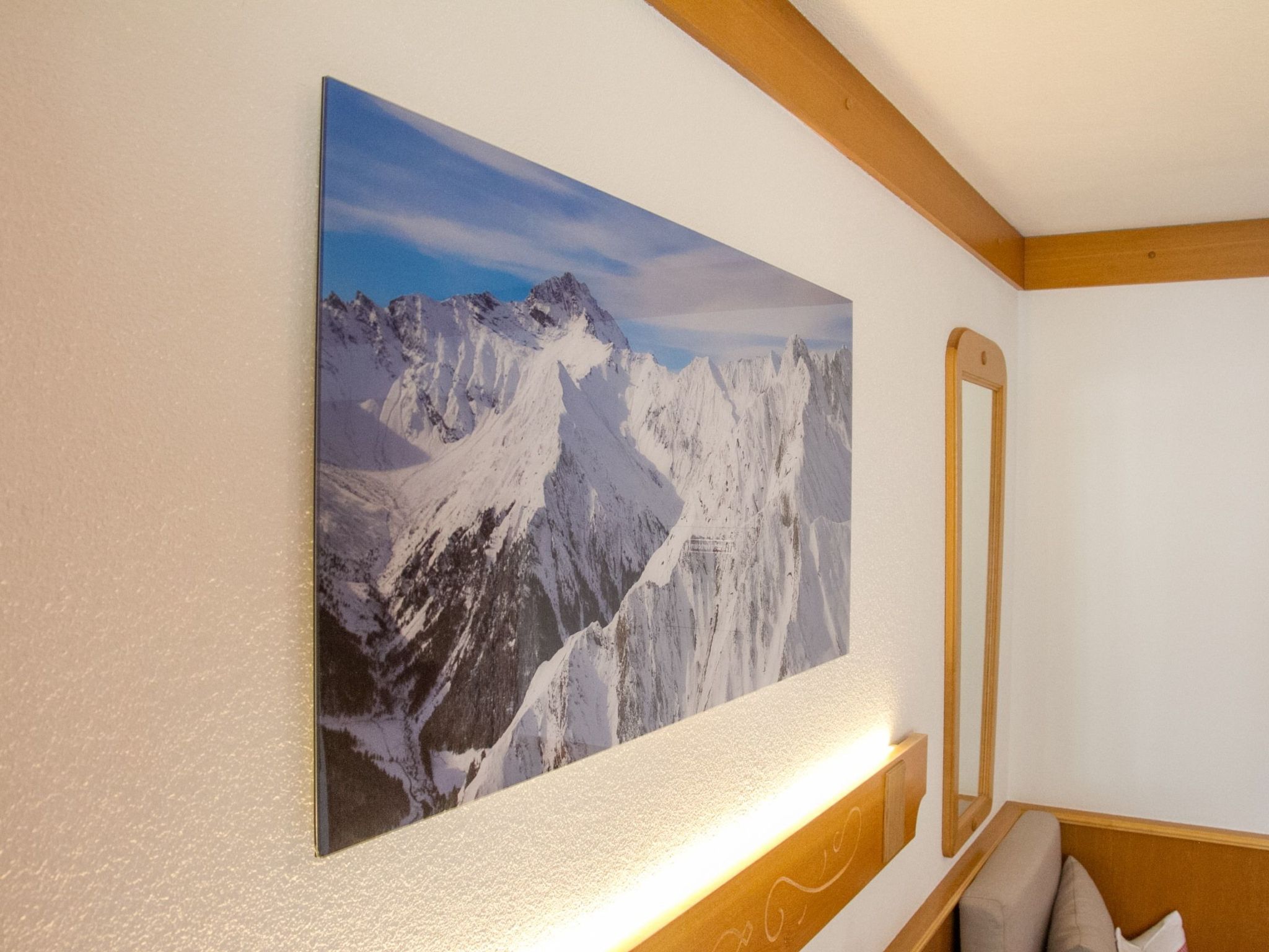 A room with a large mountain landscape painting on the wall, a wooden headboard, and a mirror.