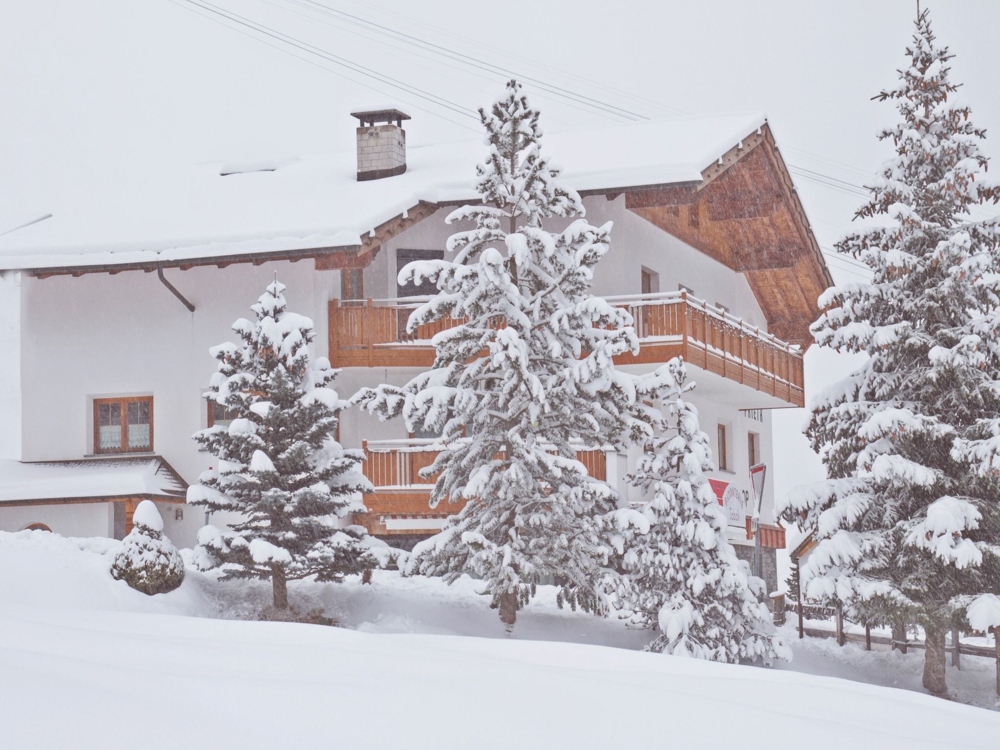 Un edificio cubierto de nieve con un balcón de madera y árboles cargados de nieve.