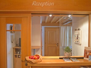 A reception area with a wooden counter, a basket of apples, a pineapple, and a framed picture on the wall. - Apart Prieth Samnaun, (Samnaun-Ravaisch) by Interhome (Samnaun)