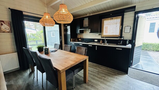 Een moderne keuken met zwarte kastjes, een houten eettafel en twee hangende rieten kroonluchters.