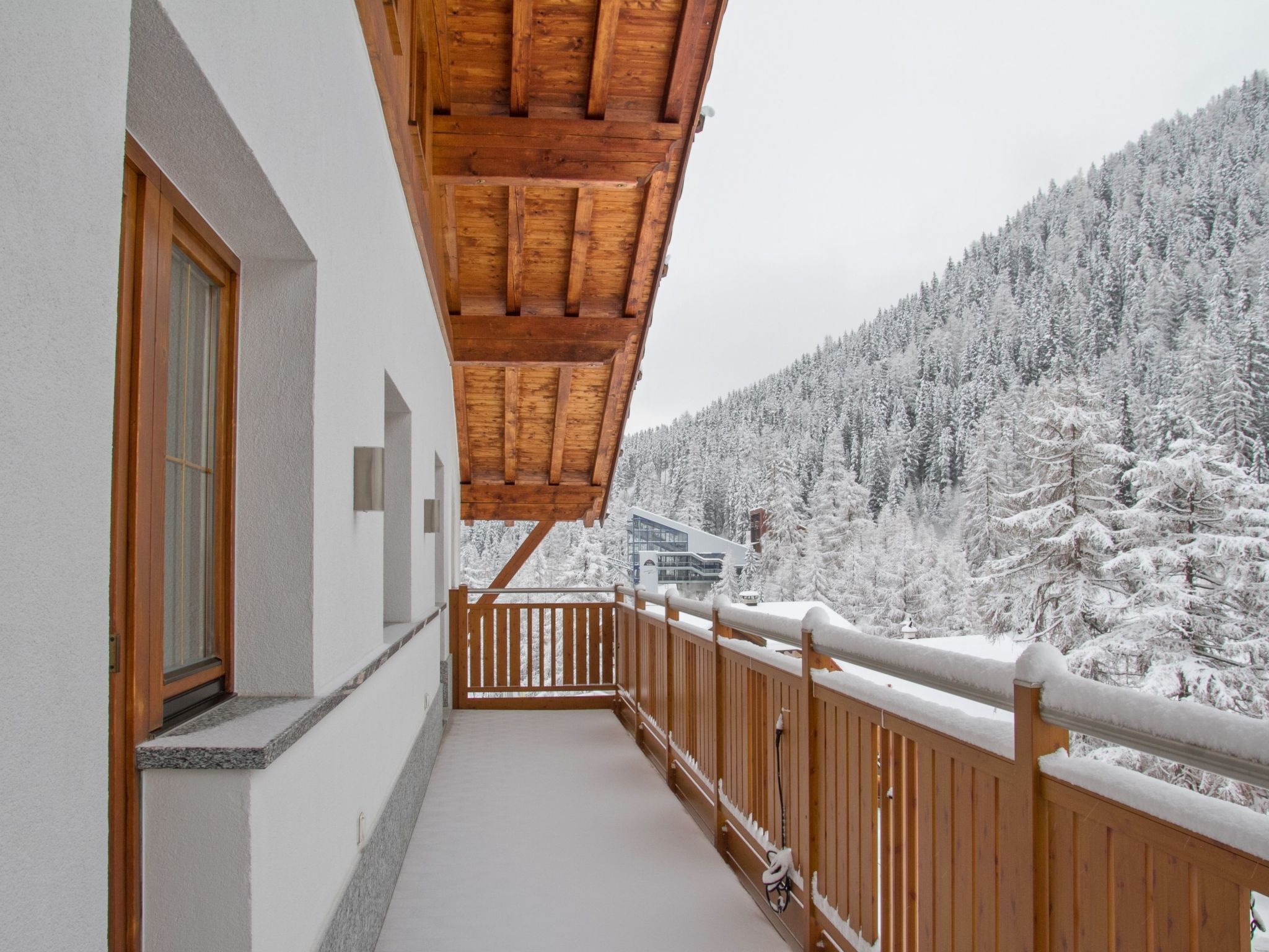 A balcony with a wooden railing overlooking a snowy forest.