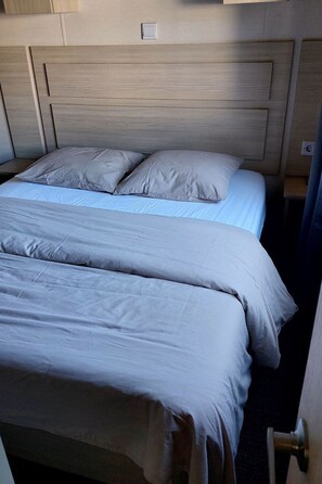 Ein Doppelbett mit Holz-Kopfteil, einer hellblauen Tagesdecke und zwei Kissen.