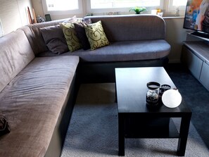 Ein Wohnzimmer mit grauem Sofa, einem schwarzen Couchtisch und einem Fernseher.