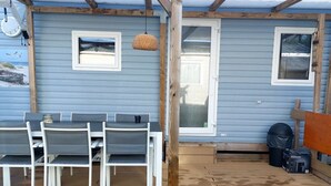 Een overdekt terras met een tafel, stoelen, een houten terras en een deur naar de binnenruimte.