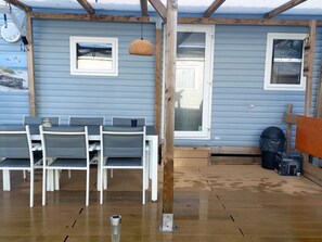 Un área de estar al aire libre techada con una mesa y sillas, una terraza de madera y una puerta que da a un espacio interior.