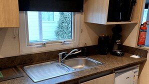 Een keuken met raam, spoelbak, koffiezetapparaat en brandblusser.