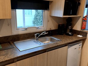 Una cocina con ventana, un lavamanos, una cafetera y un extintor.