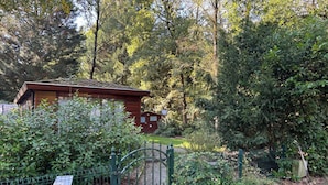 Eine rustikale Holzhütte, umgeben von dichtem Grün, einem Metalltor und einem solarbetriebenen Lichtmast.