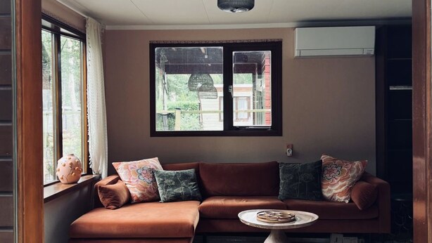 Ein gemütliches Wohnzimmer mit einem braunen Ecksofa, einem runden Holztisch und einem gemusterten Teppich.