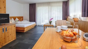 Una camera d'albergo con un letto, una TV, un armadietto in legno, un tavolo da pranzo con pane e una tazza, e una sedia.