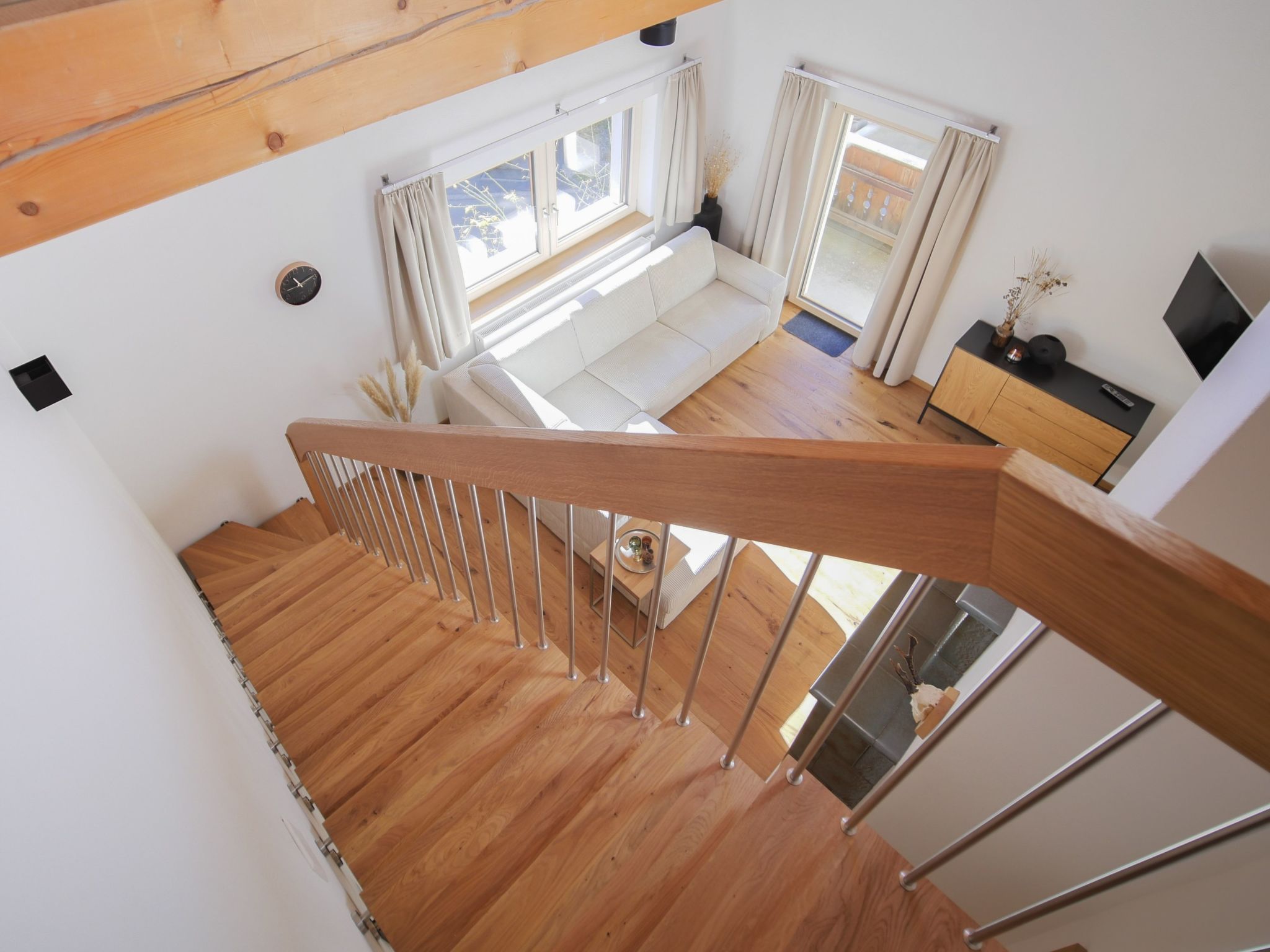 A wooden staircase leading to a living area with a sofa, a TV, and a window with curtains.