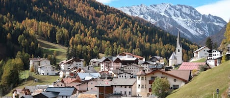 Ein Bergdorf mit traditionellen Holzhäusern, einer Kirche und einem schneebedeckten Berg im Hintergrund.