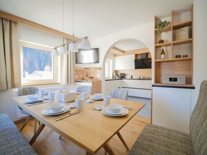 A modern kitchen with a dining area, wooden beams, and a view of the outdoors. - APARTMENT BERGWALDZAUBER – Haus zur Post, (Samnaun-Compatsch) by Interhome (Samnaun)