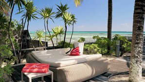 A sunlit outdoor lounge area with a cushioned seating arrangement, a small table, and a decorative pillow. - Cape Point Seafront Suites & Penthouses by LOV (Cap Malheureux)