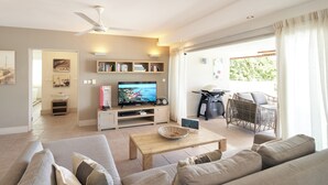 A living room with a TV, sofa, coffee table, and a balcony with wicker furniture. - Cape Point Seafront Suites & Penthouses by LOV (Cap Malheureux)