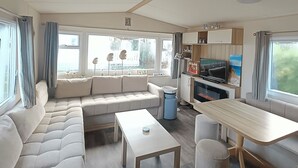Interior modern d'un autocaravana amb un sofà modular, una taula de dinar i una zona de televisió.