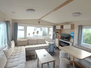 A modern RV interior with a sectional sofa, a dining table, and a TV area. - RBR 1152 - Beach Resort Kamperland by Interhome (Kamperland)