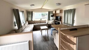 Interior d'una caravana amb un saló, taula de dinar, televisió i petita cuina.