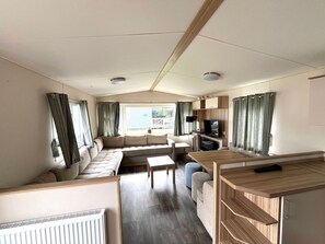 A caravan interior with a sofa set, a dining table, a TV, and a kitchenette. - RBR 1152 - Beach Resort Kamperland by Interhome (Kamperland)