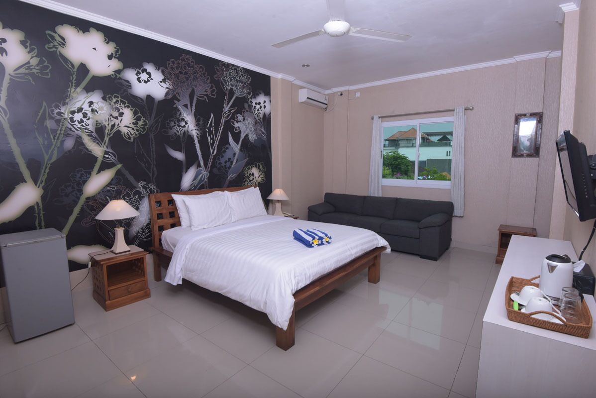 A bedroom with a bed, a desk, a chair, a TV, a window, and a wall with a floral mural.