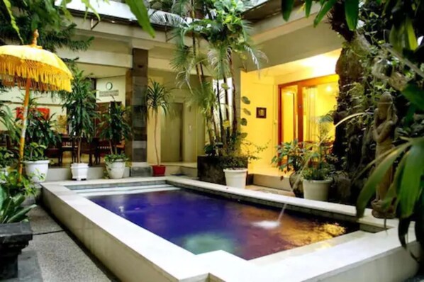 An indoor swimming pool surrounded by potted plants and a yellow wall.