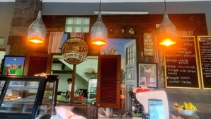 L’intérieur d’un restaurant est agrémenté de luminaires suspendus, d’une enseigne sur laquelle on peut lire : « Les personnes qui aiment manger sont toujours les meilleures », et d’un tableau affichant la carte, avec une liste de jus pressés et de divers plats.