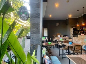 A cafe with outdoor seating, a signboard, and a view of the street.