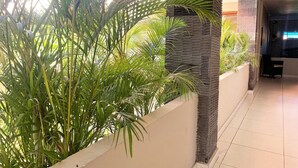 Un couloir doté d’un sol carrelé, d’un mur orné d’un élément vertical texturé et de plantes vertes luxuriantes.