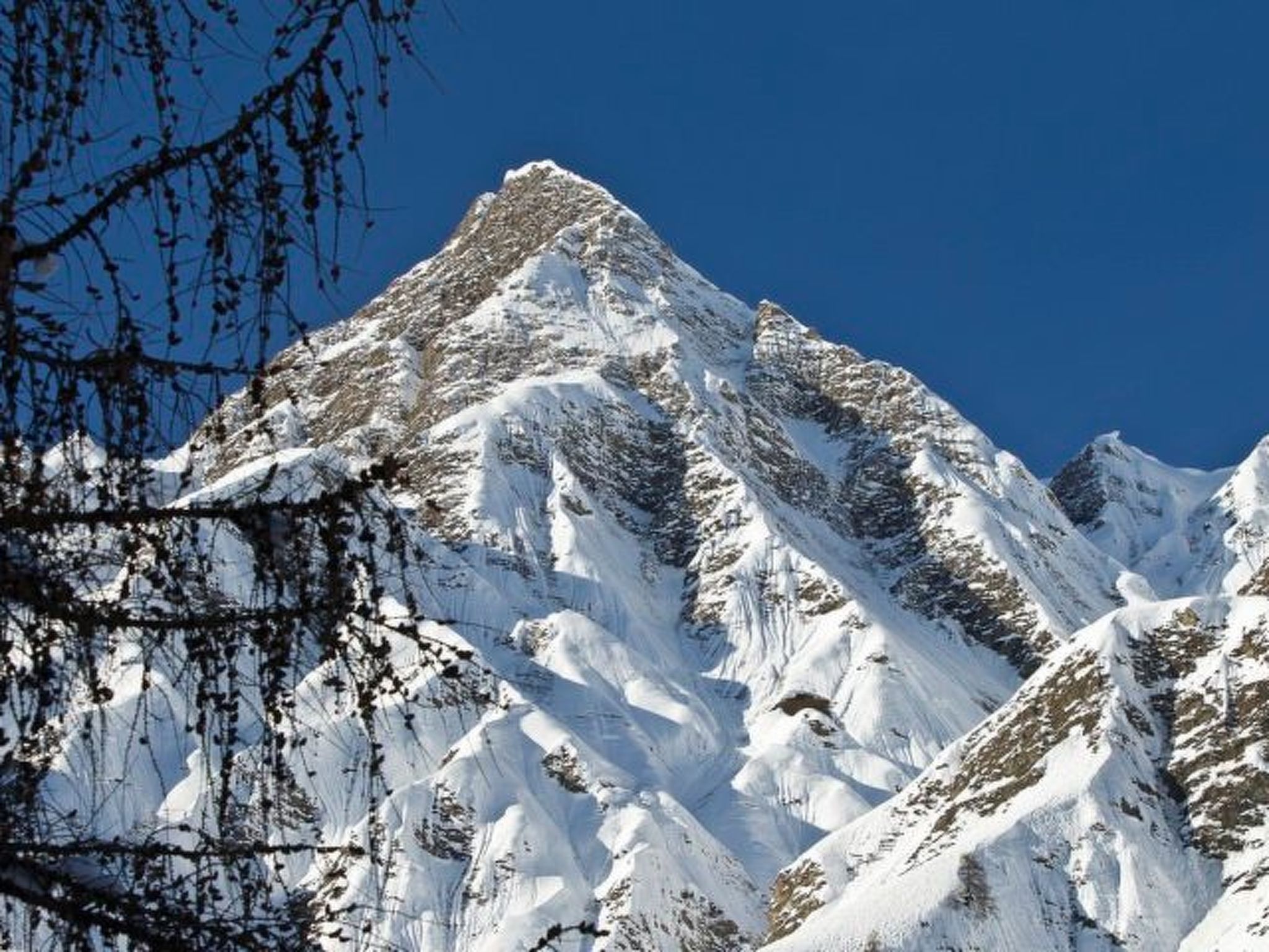 Ein mit Schnee bedeckter Berggipfel mit zerklüftetem Gelände und spärlicher Vegetation.
