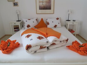 A neatly made bed with a floral pattern and orange accents, flanked by matching pillows and folded blankets. - Apartment MEZPRA142, (Samnaun-Compatsch) by Interhome (Samnaun)