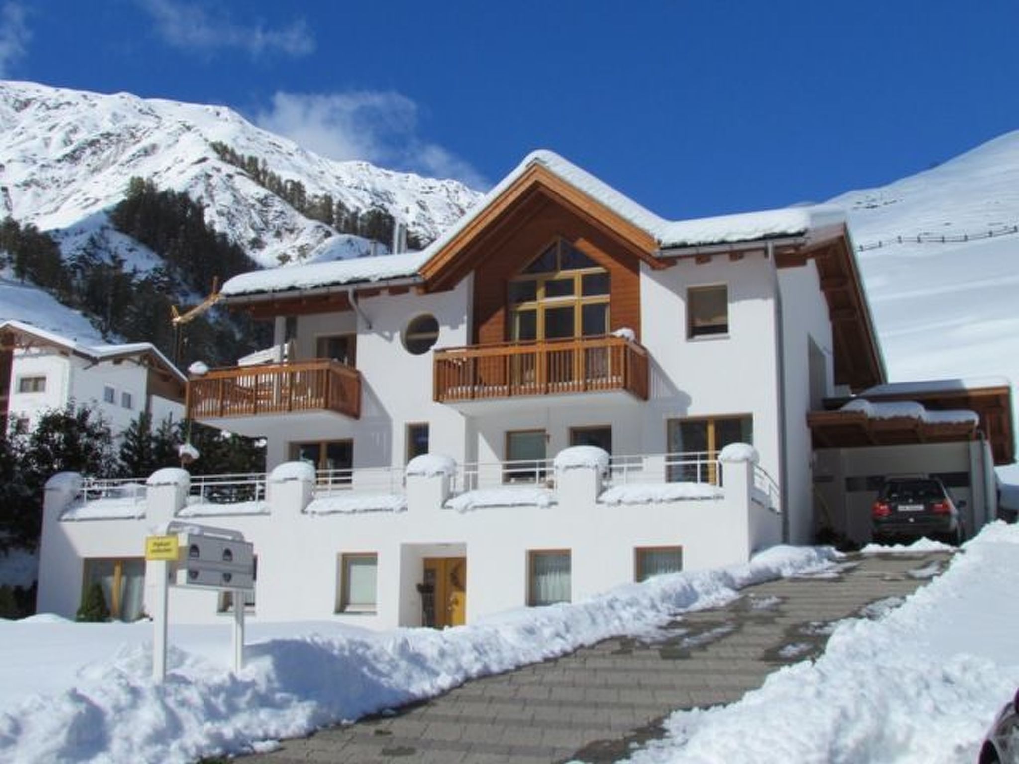Un chalet de dos pisos con balcón, garaje y un paisaje de montaña nevada.