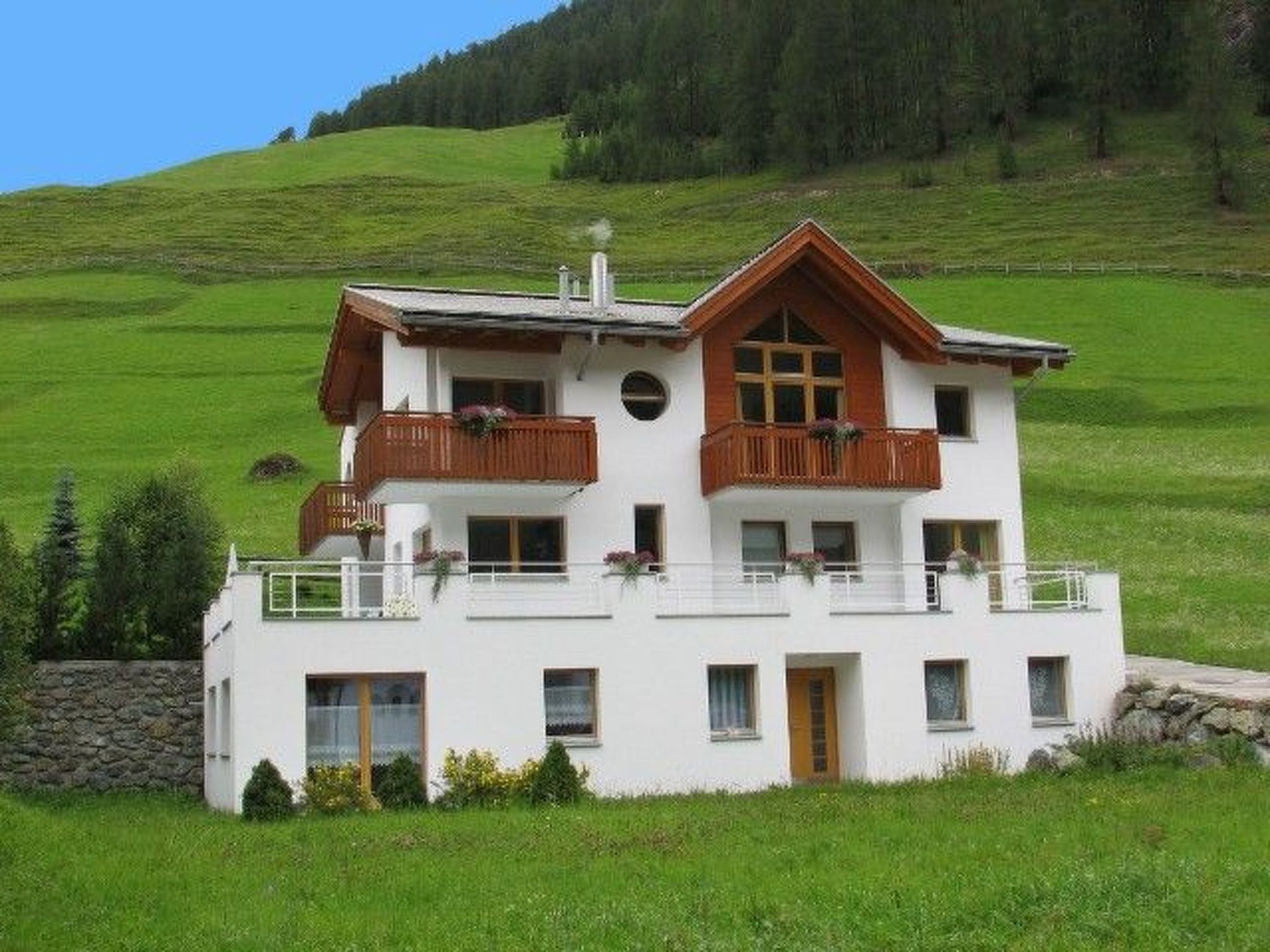 A two-story chalet with a balcony, set in a green valley.