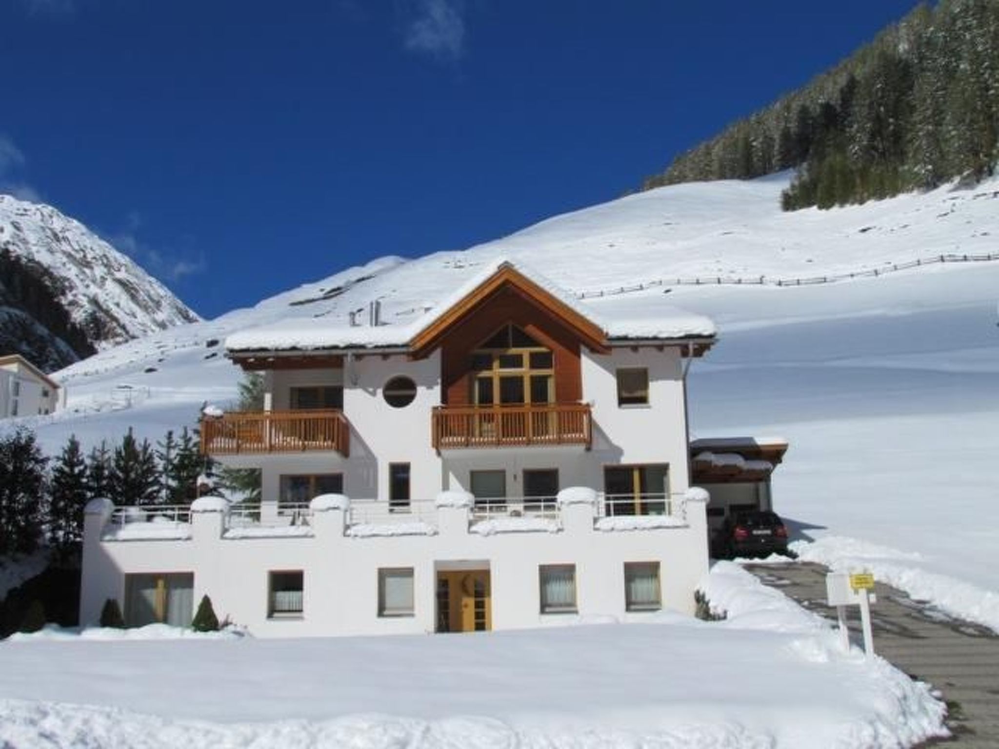A two-story chalet with a balcony, surrounded by snow-covered mountains.