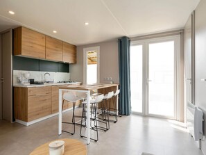 Eine moderne Küche mit Holzausstattung, ein Essbereich mit weißen Stühlen und ein großes Fenster mit Vorhängen.