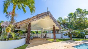 Zona de piscina con una estructura de techo de paja, piscina y zona de bar.