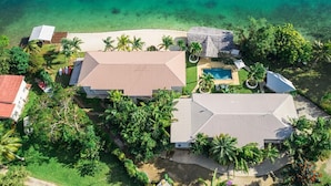 Vista aérea de una propiedad costera con una casa grande, una piscina y una playa.