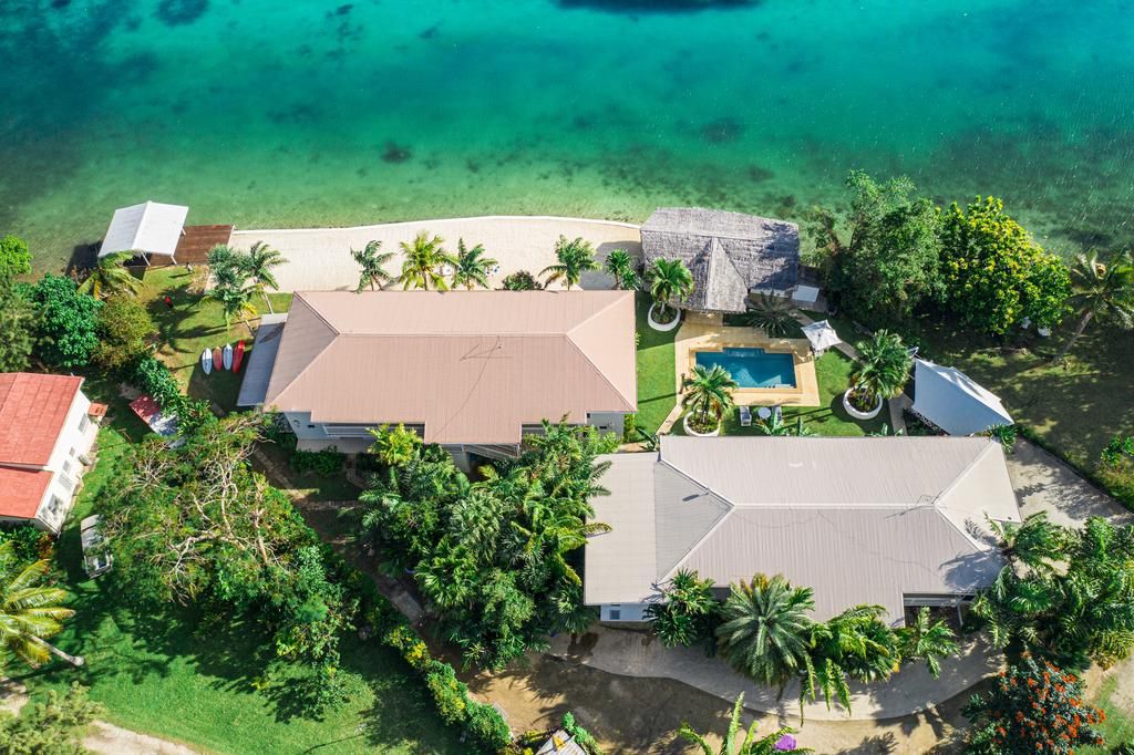 Vista aérea de uma propriedade costeira com uma casa grande, piscina e praia.
