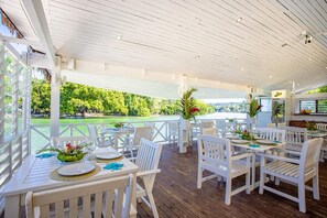 Een terras buiten met witte houten meubels, uitzicht op een golfbaan, en een restaurantgedeelte met een balie.