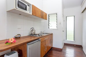 A kitchen with wooden cabinets, a stainless steel refrigerator, a microwave, and a gas stove. - Tropicana Lagoon Resort (Port Vila)