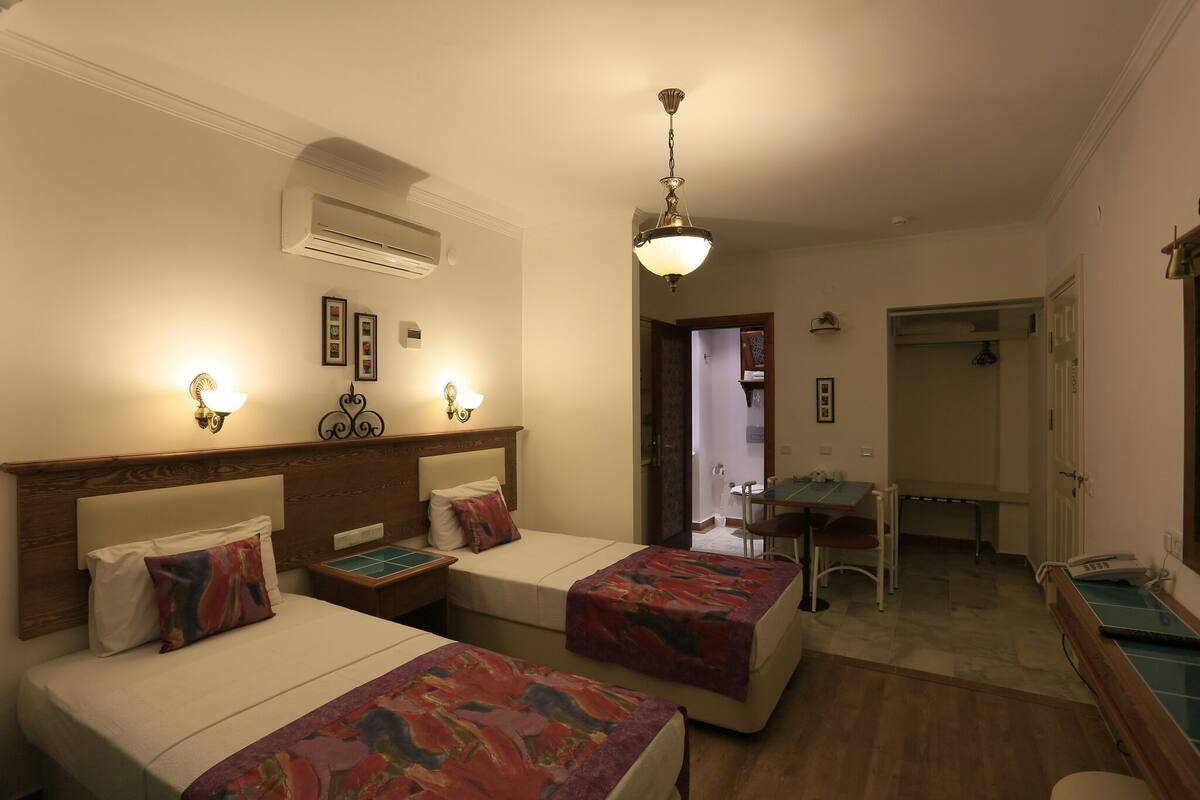 A hotel room with two beds, a desk, a chair, an air conditioning unit, and a telephone.