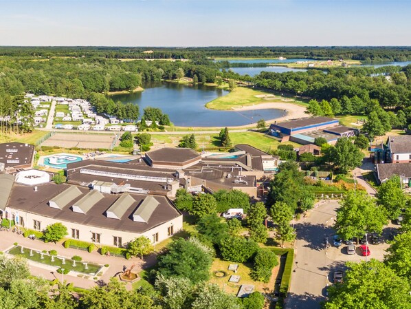 Ein großes Gebäude mit mehreren Dächern, umgeben von viel Grün und einem See.