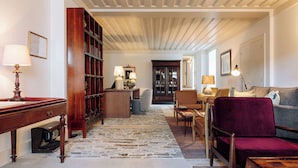 A spacious living room with a wooden bookshelf, a red armchair, a grey sofa, and a patterned rug. - Quinta Nova Winery House Relais & Châteaux (Santa Maria da Feira)