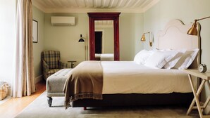 A neatly arranged bedroom with a bed, a chair, a bedside table with a lamp, and a wall-mounted air conditioner. - Quinta Nova Winery House Relais & Châteaux (Santa Maria da Feira)