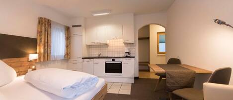 Quarto de hotel com cama, escrivaninha, cadeira, cozinha compacta e banheiro.