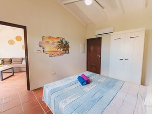 Une chambre avec un lit, un mur orné d’une fresque aux motifs tropicaux, une porte en bois et une armoire blanche.