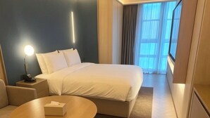 Habitación de hotel con cama, mesita de noche, silla y vistas al exterior.