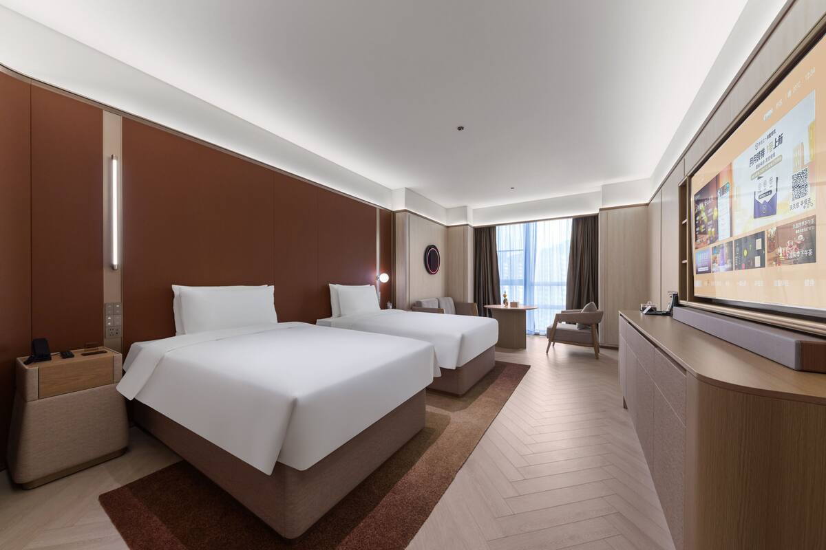 Une chambre d’hôtel avec deux lits, un bureau, une chaise et une grande fenêtre.